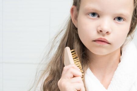 little girl combing hair with a wooden comb, portraitの写真素材