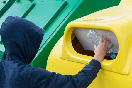 a child in the hood throws an empty bottle in a yellow container intended for plastic waste