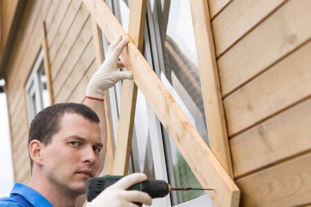 a man with a screwdriver in his hand is blocking the windows of the house with boardsの写真素材