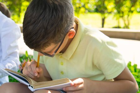 close-up, in the park, in the fresh air, a schoolboy enthusiastically does a task on arithmeticの写真素材