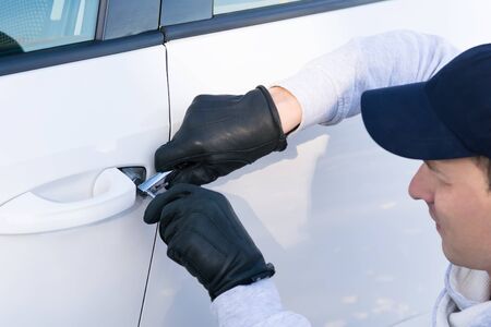 a thief in a cap wants to break the lock in the door of a white car, close-up