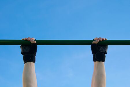 close-up of a man's hands in gloves playing sports on a horizontal bar against a blue sky