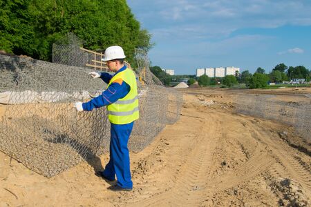 the Builder in a yellow vest and a white helmet, opens a box of mesh to check the designの写真素材
