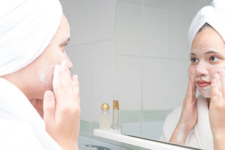 acne care teenager in a bathrobe standing in the bathroom in front of the mirror