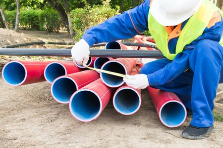 worker measures red plastic pipes front view