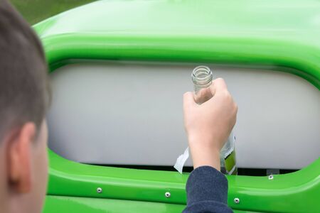 a boy throws an empty glass bottle into a special container for glass, close-upの写真素材