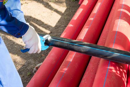 worker cuts a plastic pipe with special scissors at a construction site