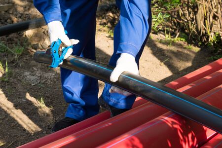 worker cuts a piece of plastic pipe with special scissors