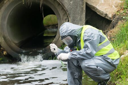 a man in a protective suit takes a sample of water from the river after the release of chemical wasteの写真素材