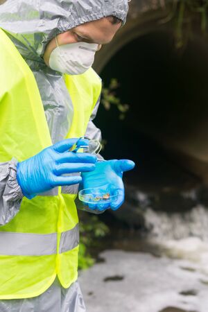 scientist in yellow protective vest and mask, uniform and gloves, closes the Petri dish, after collecting materials, close-upの写真素材