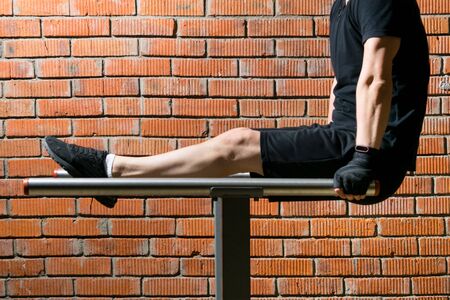 close-up, against the background of an orange brick, a man in black uniform is engaged in gymnastics, on the uneven barsの写真素材