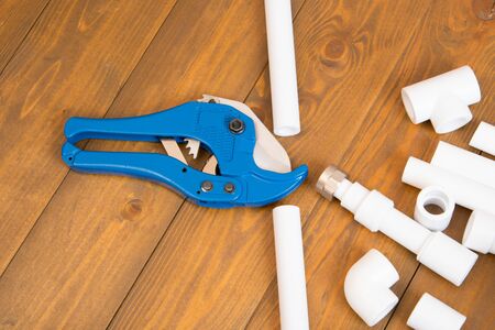 blue scissors for cutting plastic pipes, next to the corners and adapters for them, on a wooden backgroundの写真素材