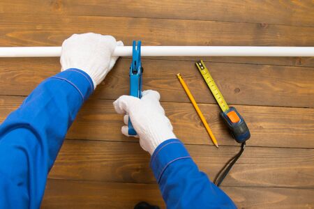 on a dark wooden background, the hands of a worker in white gloves, cut a polypropylene pipe with...