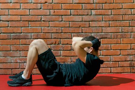 against the background of an orange brick, a man in black uniform, plays sports, doing lying,...