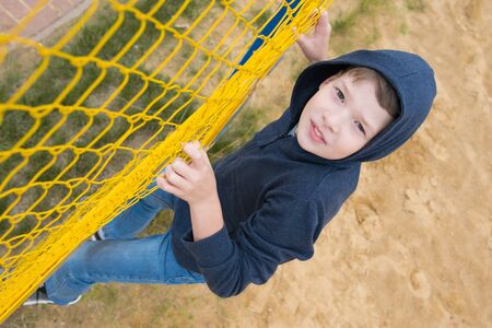a boy in a blue jumper with a hood, climbs on a yellow grid, upの写真素材