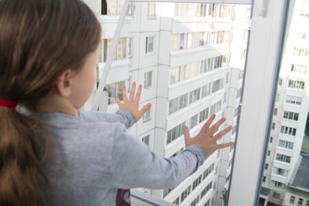 child girl, close-up, pushes a mosquito net out of the window, a dangerous situation, against the background of the houseの写真素材