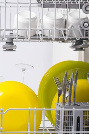 Green and yellow plates are in the basket of the dishwasher, close-upの写真素材