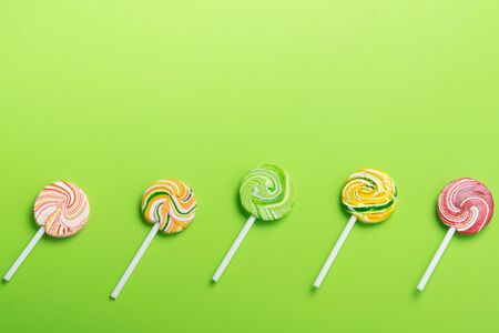 colorful lollipops on a stick, neatly arranged in a row, on a light green background, there is a...