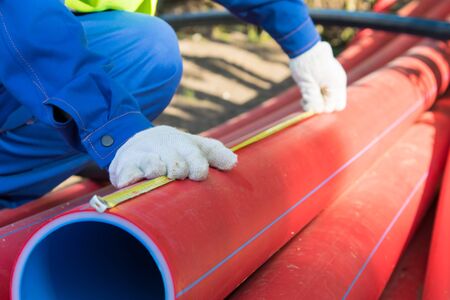 builder's hands in white gloves, measure the length of the red plastic pipe, yellow tape measure, to mark the size, close-upの写真素材