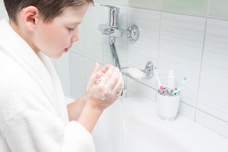 a boy in a white coat washes his hands with soap in the bathroomの写真素材