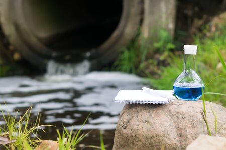 close-up of a flask with a blue reagent and a notebook with a pen against the background of the...