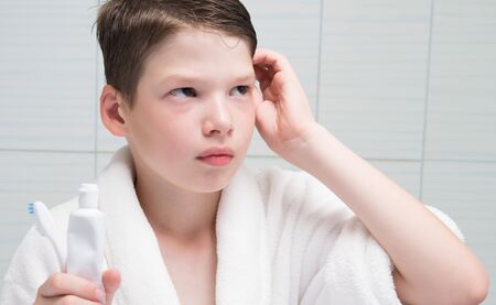 boy, in a white coat, in the bathroom, holds in his hand a toothbrush and paste, thoughtの写真素材