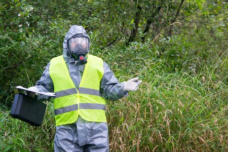 a specialist in a protective suit and mask, with a suitcase and a tablet, spreads his hands and can...