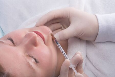 doctor in sterile gloves, gives a beauty injection to a woman, in part of the chin