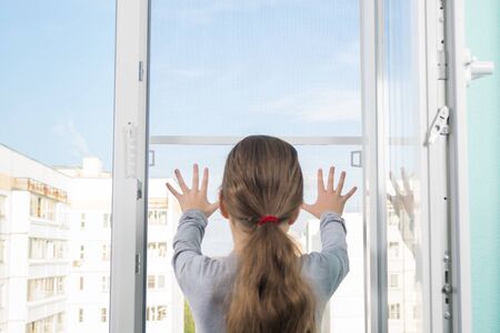 the girl dangerously put her hands on the loosely fixed mosquito net of the window, the danger of falling out of the windowの写真素材