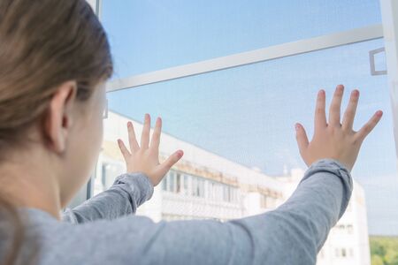 the girl dangerously put her hands on a loosely fixed mosquito net window, the danger of falling from the window, close-upの素材 [FY310141126622]