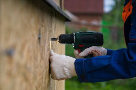 worker drilling wooden boards in the lower part of the house, close-up