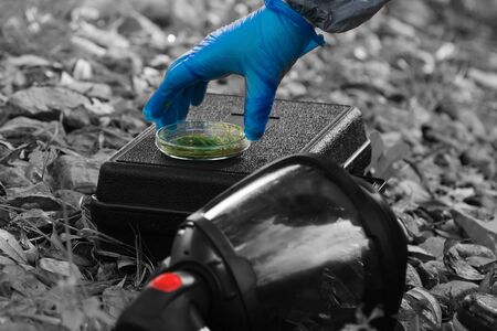 hand in a blue glove holds a glass container with green grass on a suitcase, black and white photo