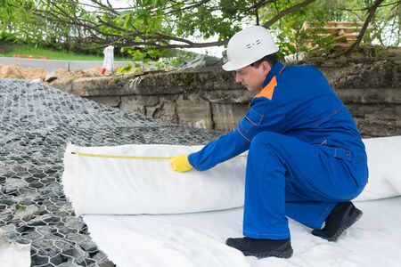 a worker in a workwear hides with a special cloth the bottom of an artificial lake, side view