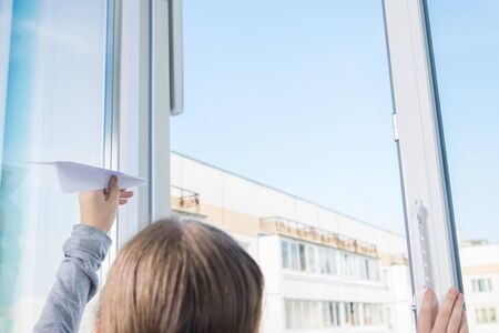 child launches a paper airplane through the window of an apartment on the street, close-up