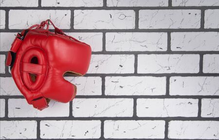 protective red Boxing helmet, hanging on a hook , against a white brick wall, there is a place for the inscriptionの写真素材