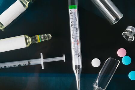 against the background of a photograph of a person with suspected coronavirus, a syringe with a drug, multi-colored tablets, ampoules, a thermometer for measuring body temperature, close-upの写真素材