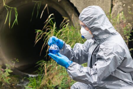 a man in a protective suit and mask holds in his hands a flask with a blue liquid on the background...