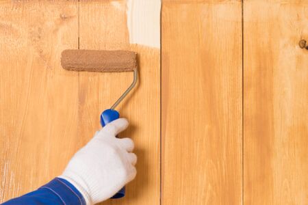 roller paints the last uncoated area on a wooden wall
