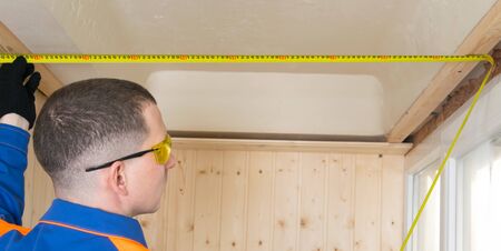 master in a blue uniform and black gloves, measures the distance with a yellow meter, between the window and the wall, close-upの写真素材