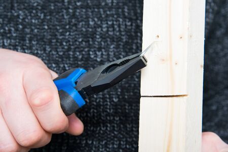 close-up, hand of a worker with pliers, pulling a metal nail from a wooden barの写真素材
