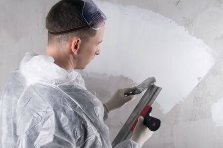 close-up, rear view of a person working on leveling the walls, applying the solution to the spatula