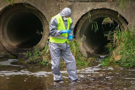 a man in a protective suit and mask took a soil sample from the bottom of the river into a Petri...