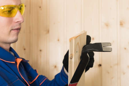 male construction worker in safety glasses pulls a nail from the board with a special tool
