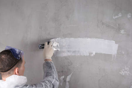 a man in special clothes conducts plastering work on the wall, back viewの写真素材