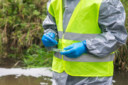 a man in a protective suit takes soil samples into a Petri dish from treatment facilities, close-upの写真素材
