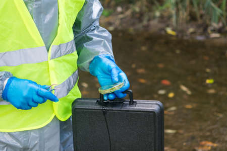 in the hands of plant samples from the river and its surroundings by a man in a special suit, side...