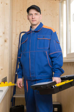 a man in special clothes with a tool for repairing apartments stands on a background of a wooden...