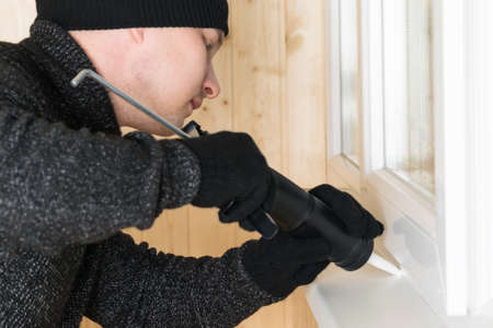 a man in clothes for repair makes sealing of cracks of plastic windows with the help of white selicon and a special toolの写真素材