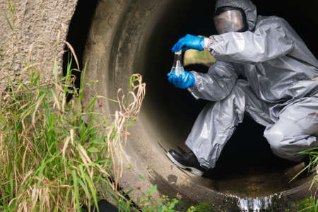 a man in a protective suit and mask in a large sewer took a sample of water for analysisの写真素材
