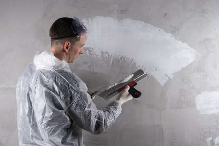 a man with a spatula repairs a wall with plasterの写真素材